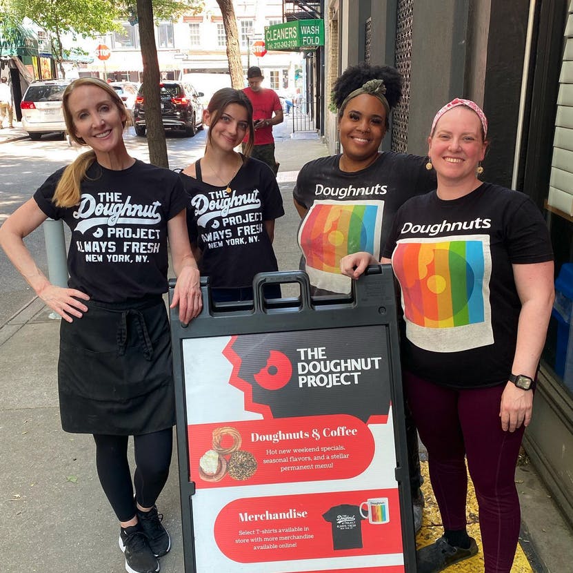 four women posing for the camera wearing doughnut project shirts