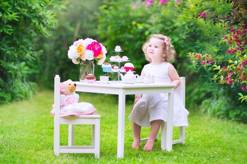Toddler girl playing tea party with a doll