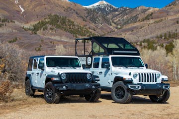 Two white jeeps are parked next to each other in front of a mountain