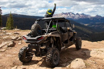 Man throws fist in the air while sitting in a RZR with mountains in the background