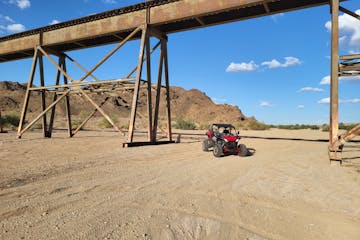 a red UTV drives underneath a railroad trestle in the California desert