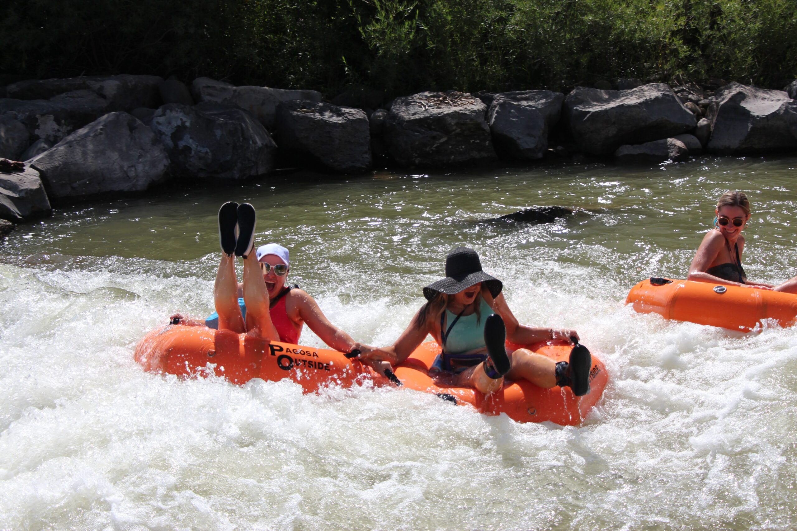 three women riding a wave on orange river tubes in the river