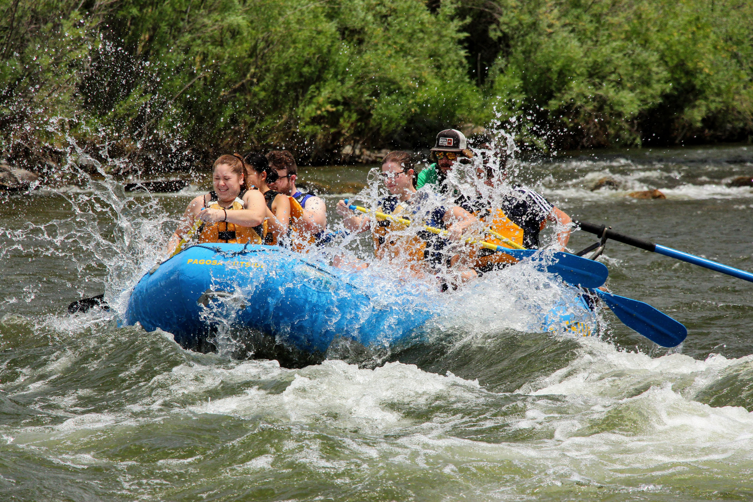 A group of rafters in a blue boat navigate through rapids