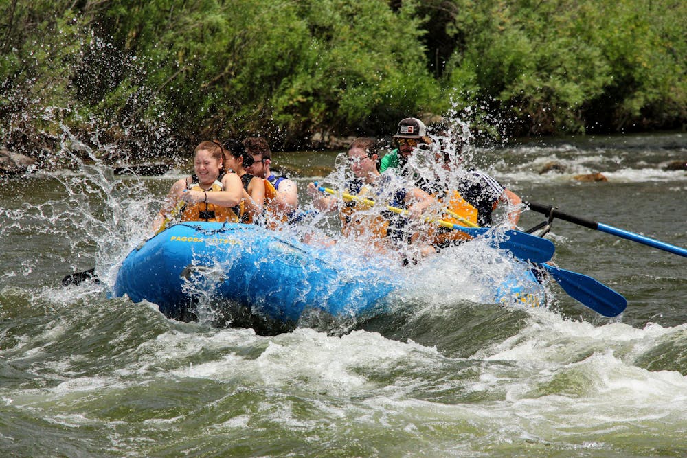 A group of rafters in a blue boat navigate through rapids