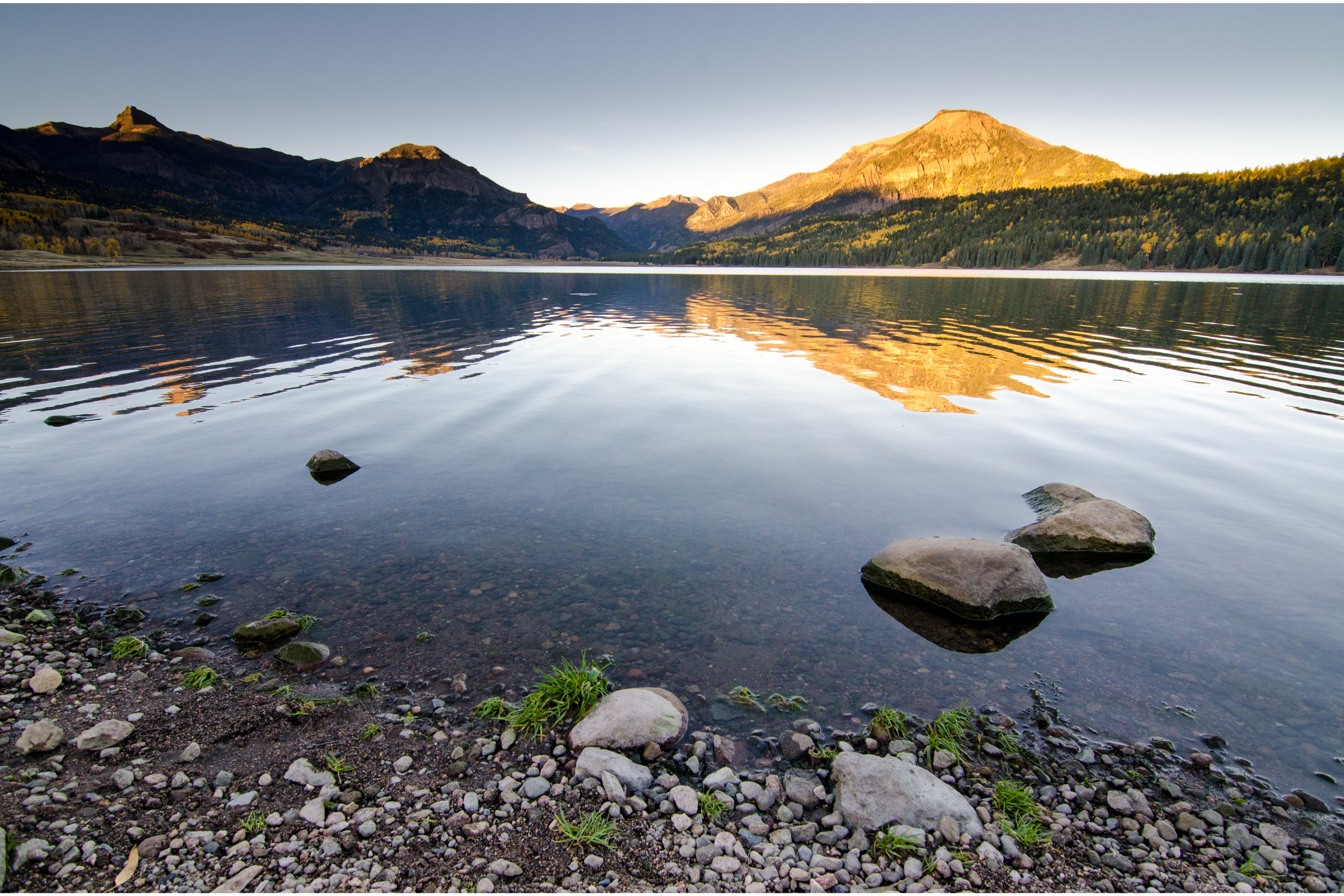 The sun setting on mountains at the far end of a remote lake