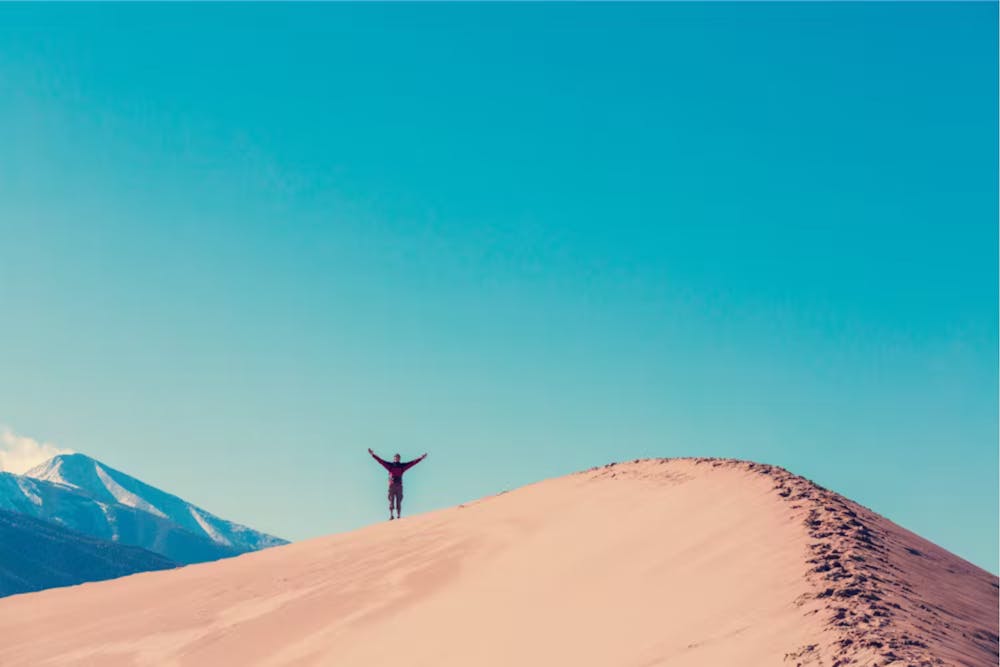 a hiker stands on a sand dune
