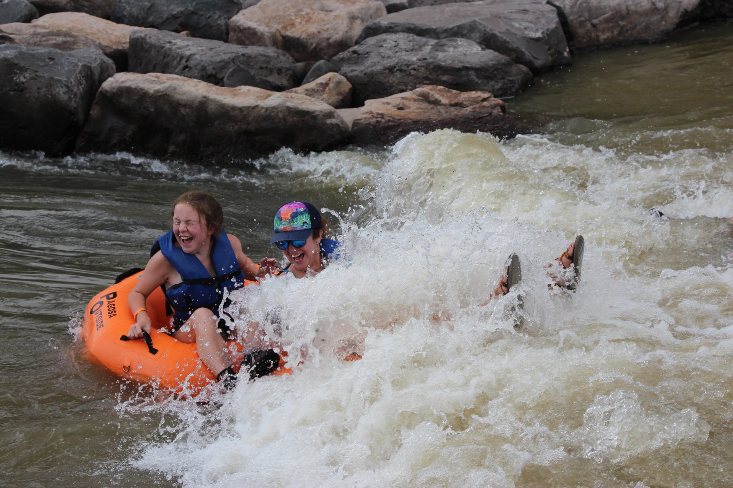 a woman and her daughter river tube through a wave