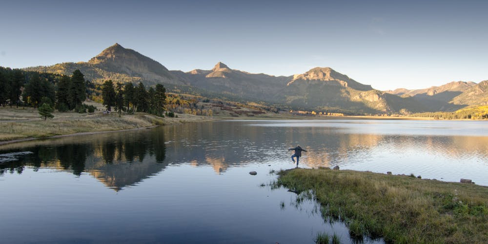 A person poses in front of an alpine lake