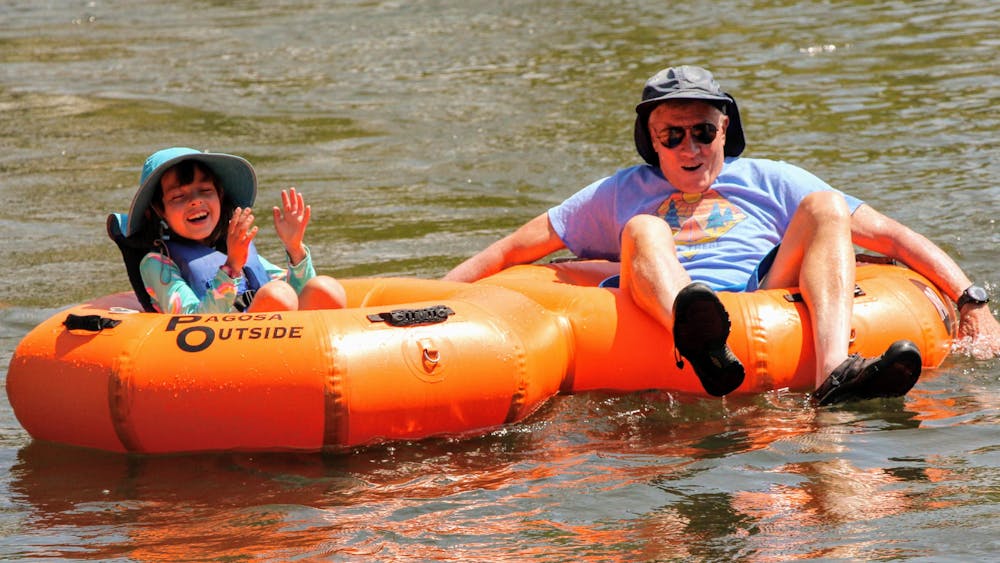a child and her grandpa sit on orange river tubes and float the river
