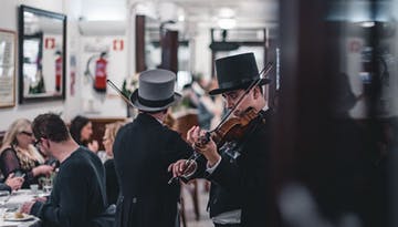 two persons playing violin while a bunch of people eating