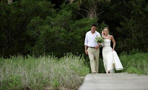 Newly married husband and wife walking down boardwalk on island