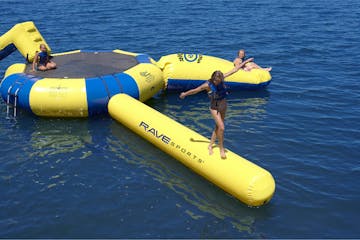 A Water trampoline floating in water with 3 girls playing on it