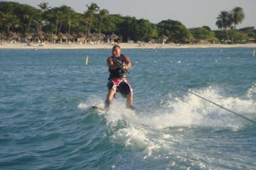 Man wakeboarding on a small wave. Palm trees and cabanas on the beach are in the background