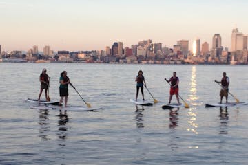 group of stand up paddle boarders in front of Seattle skyline