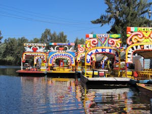 a colorful boat in the water with Xochimilco in the background