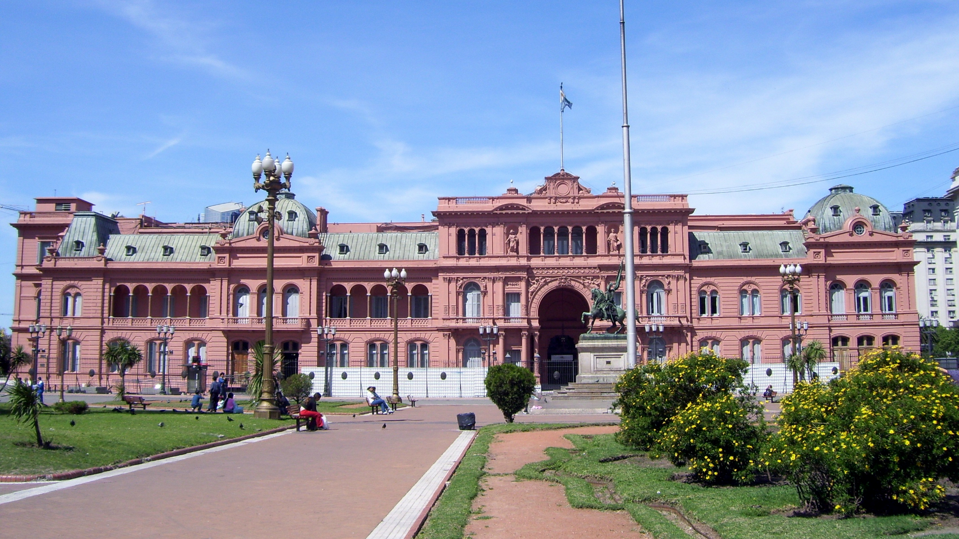 a large brick building with grass in front of a house with Casa Rosada in the background