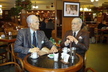 Borges and Bioy Casares (both writers)sitting at a table in a restaurant.