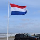 A Dutch flag on a high pole next to the beach