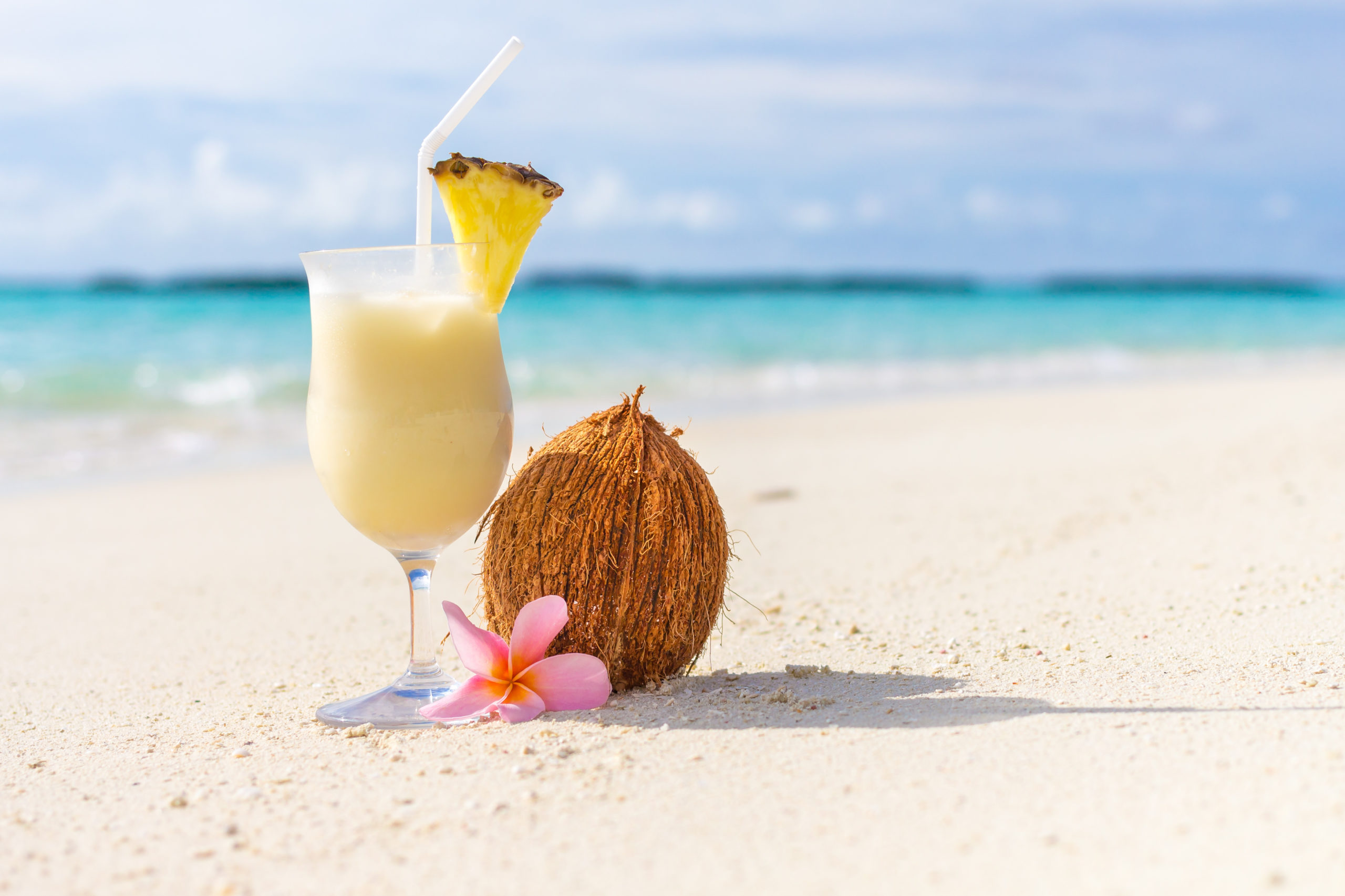 a pina colada in a glass goblet sitting on the sand next to a coconut