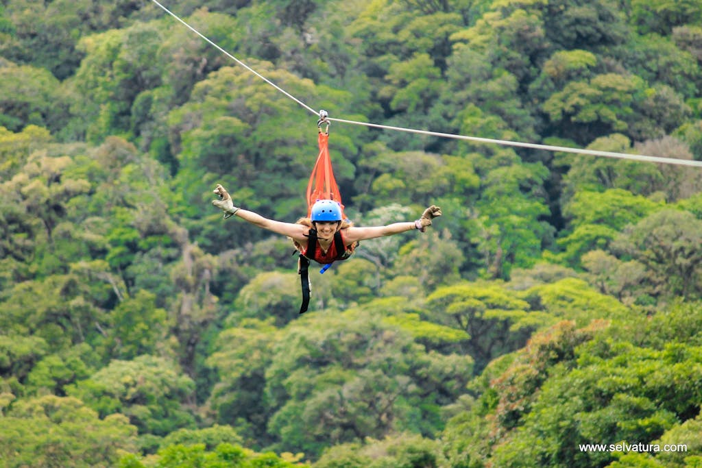 a person flying over a forest at the Superman Zip Line