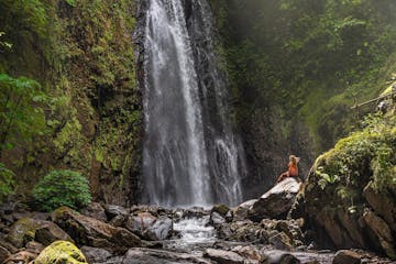 A person standing next to the largest waterfall at El Tigre Waterfalls in Monteverde, Costa Rica.