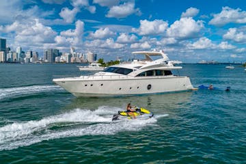 Rent a yacht in Miami Beach at anchor near Marine Stadium with a guest on a jetski nearby.