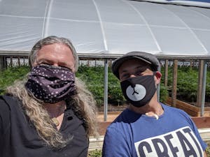 Two cannasseurs in masks in front of a weed filled greenhouse on one of the pot farms in California's Emerald Triangle