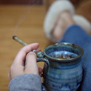 a close up of a person holding a joint and a cup