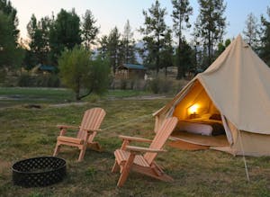 a glamping site with canvas tent and 2 Adirondack chairs by a fire pit