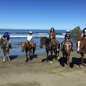 a group of people riding horses on a beach