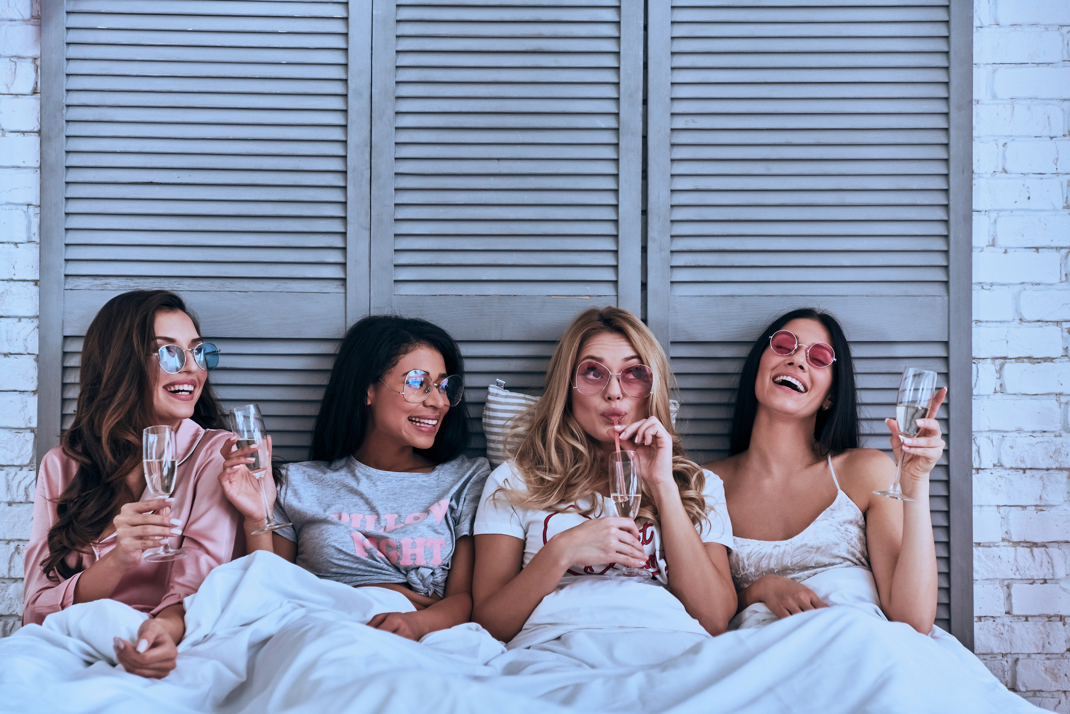 Four attractive young women in pajamas drinking cocktails and smiling while lying in the bed