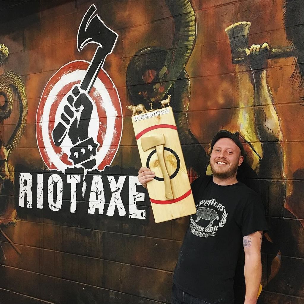 A man stands in front of Riot Axe, with a axe on a bullseye