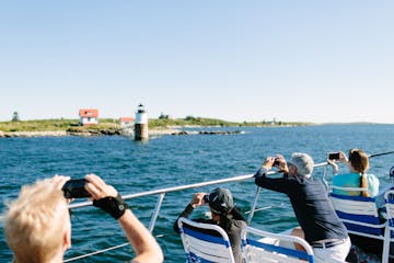 people taking photos of a lighthouse from a harbor cruise