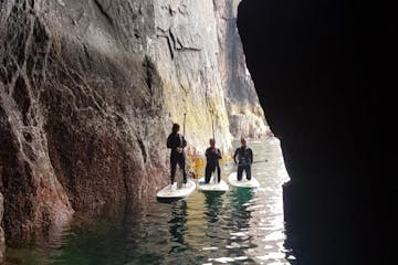three people on stand up paddle boards in a sea cave
