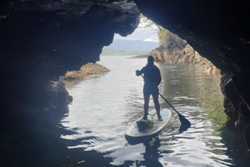 a person stand up paddler boarding into a sea cave