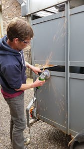 a man angle grinding rust off a metal trailer