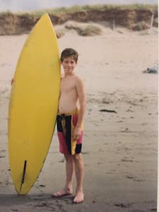 a boy standing on a beach with a yellow surf board