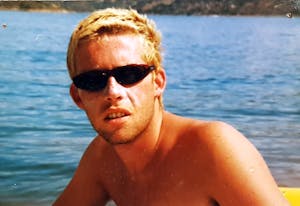 a young man in front of a body of water with sunglasses on