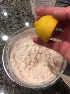 a hand holding a lemon, to be added to the other ingredients of smoked salmon dip