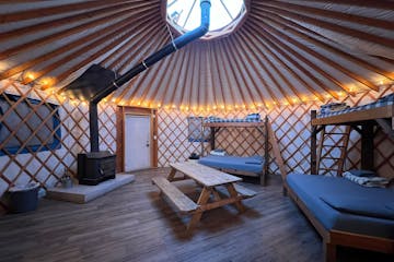 inside a Yurt with a iron stove, picnic table and 2 bunk beds