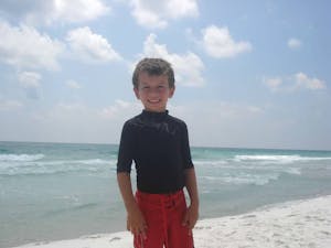 Boy wearing a black rash guard with red shorts hanging out on the pristene white sugary sand on Pensacola Beach.