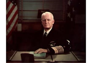 Chester W. Nimitz wearing a suit and tie sitting in front of a laptop