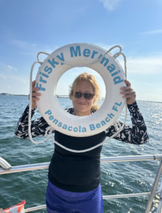 A passenger traveling alone takes advantage of the Frisky Mermaid ring buoy to snap a picture and capture a memory with her head showing through the center of the life ring.