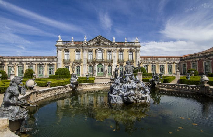 a castle surrounded by a body of water with Palace of Queluz in the background