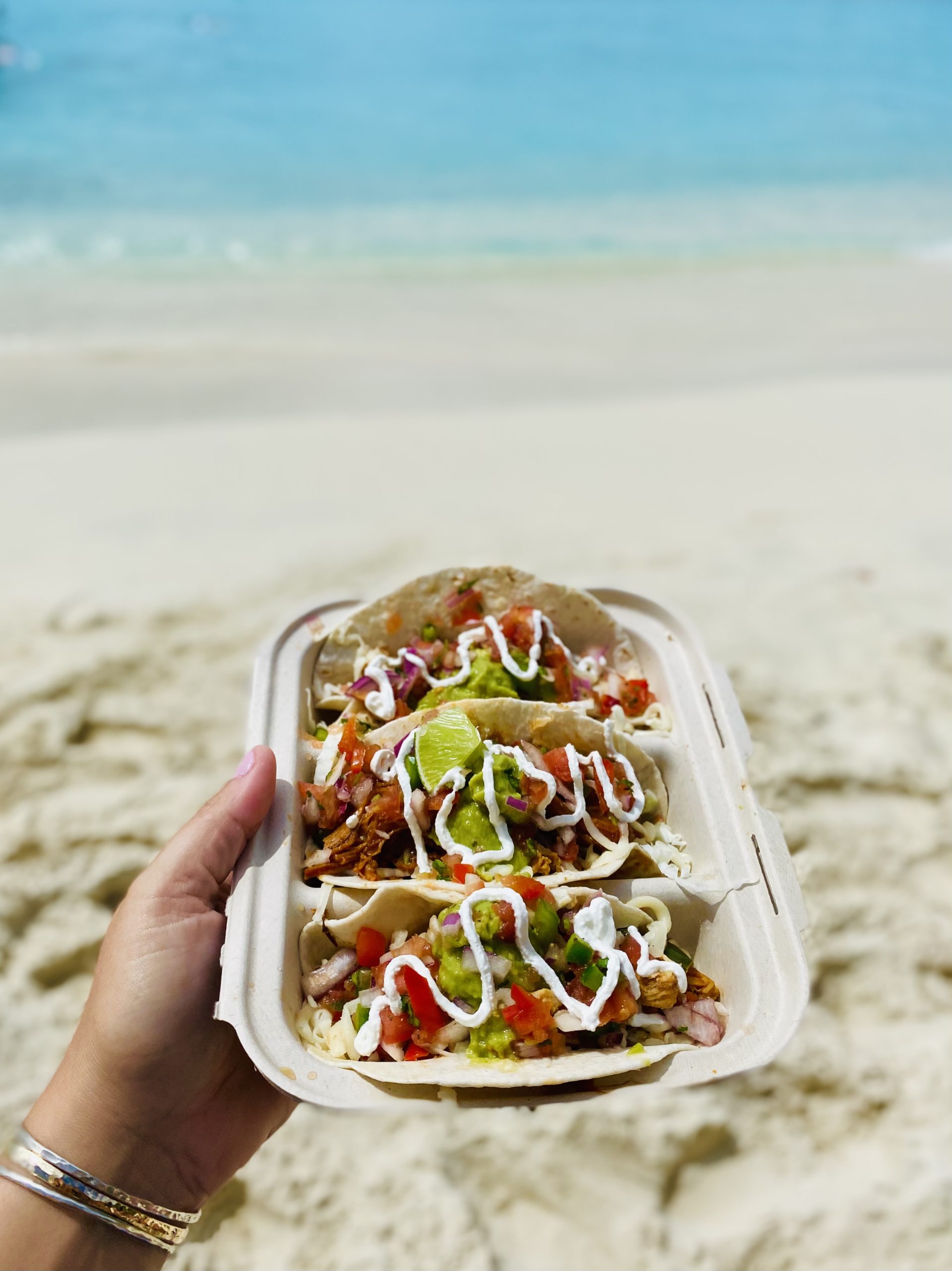 a hand holding tacos on a beach