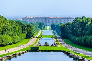 a large long train on a lush green field with Palace of Caserta in the background