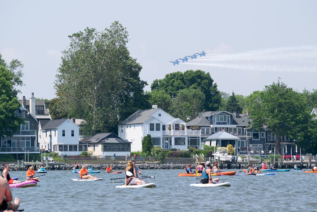 People on kayaks and paddle boards watch Navy Blue Angel jet planes fly overhead
