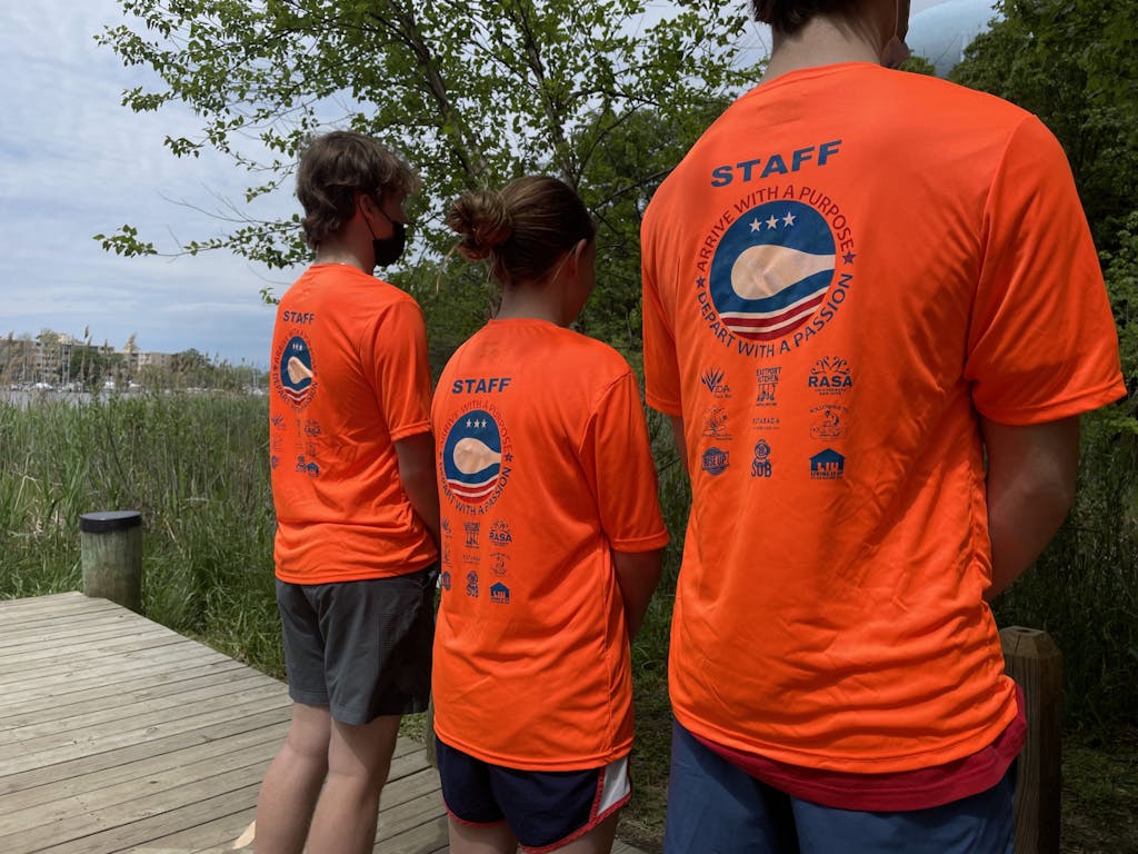 Three staff members pose to show the logos of Capital SUP partners on their tee shirts.