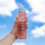 a hand holding a bottle of Rasa juice against a background of the sky