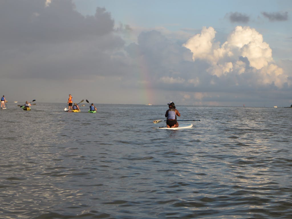 A woman on a stand up paddleboard take a picture of a rainbow on the horizon
